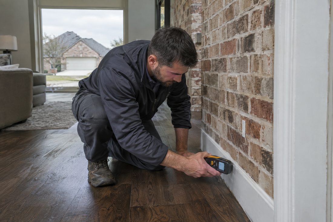 A close view of a restoration worker checking moisture along baseboards and flooring inside a Rockwall brick ranch in Rockwall, TX