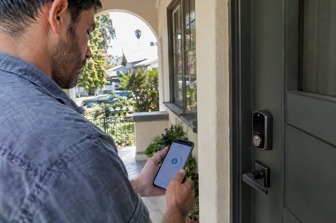 A homeowner testing a newly installed smart deadbolt with a phone app on a porch at a Mid-City Los Angeles Craftsman duplex with an arched porch in Los Angeles, CA