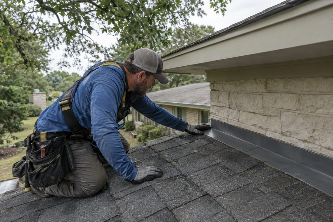 Close view of a roofer checking flashing beside shingles on a Crestview home, with leafy branches visible above the roofline in Crestview, TX