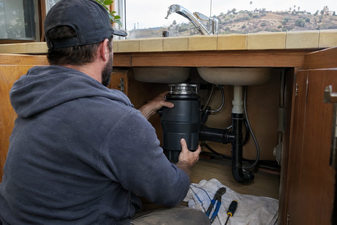 A new garbage disposal being installed under a kitchen sink at a hillside 1970s ranch home in Vista, inland San Diego County in Vista, CA